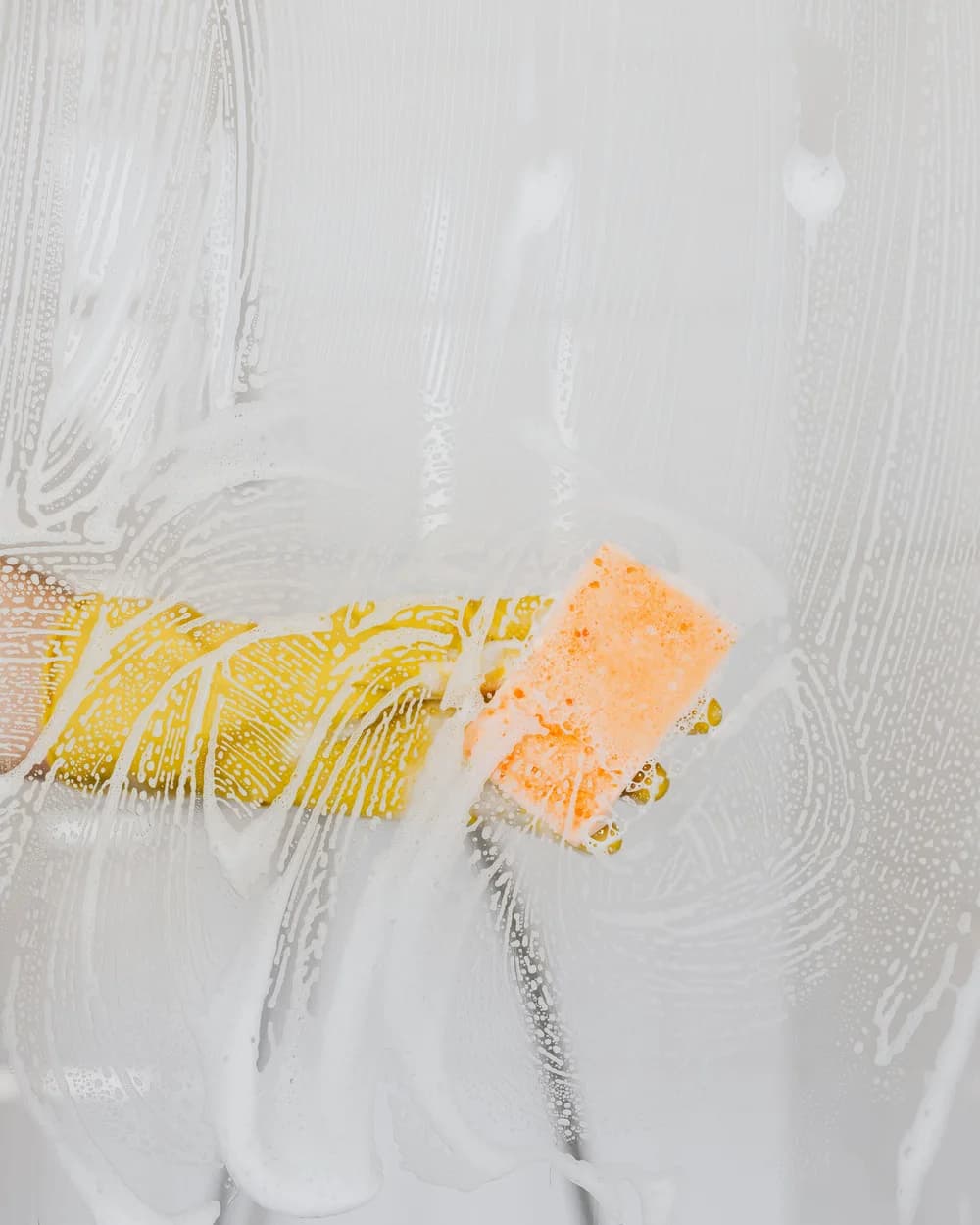 A squeegee clearing soapy foam from a glass surface during a deep clean