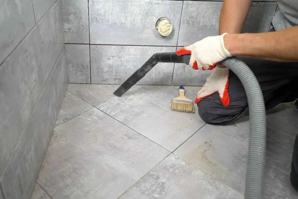 A worker vacuuming construction dust from a newly tiled floor